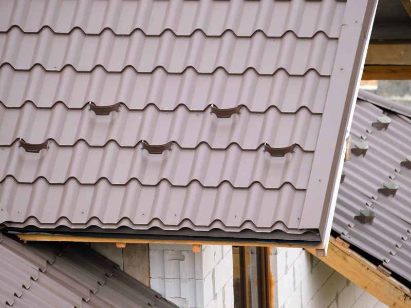 Closeup snow guard for safety in winter on house roof top covered with steel shingles. Tiled covering of building.