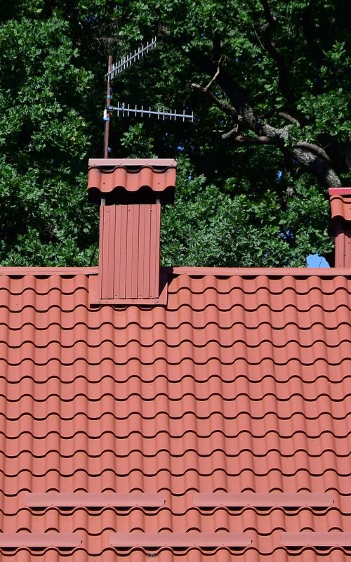 High quality red metal tile roof of a house against green trees background