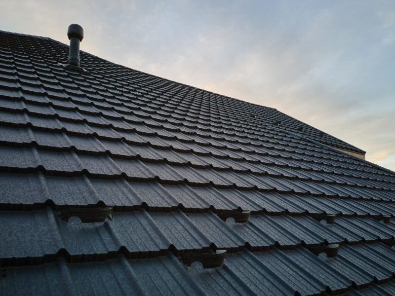 Snow guard for safety in winter on house roof top covered with steel shingles. Tiled covering of building.